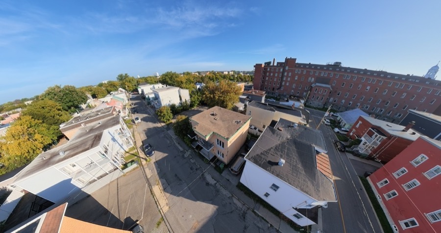 Vue aérienne d'une rue résidentielle, entre des immeubles à logements et un grand bâtiment de briques