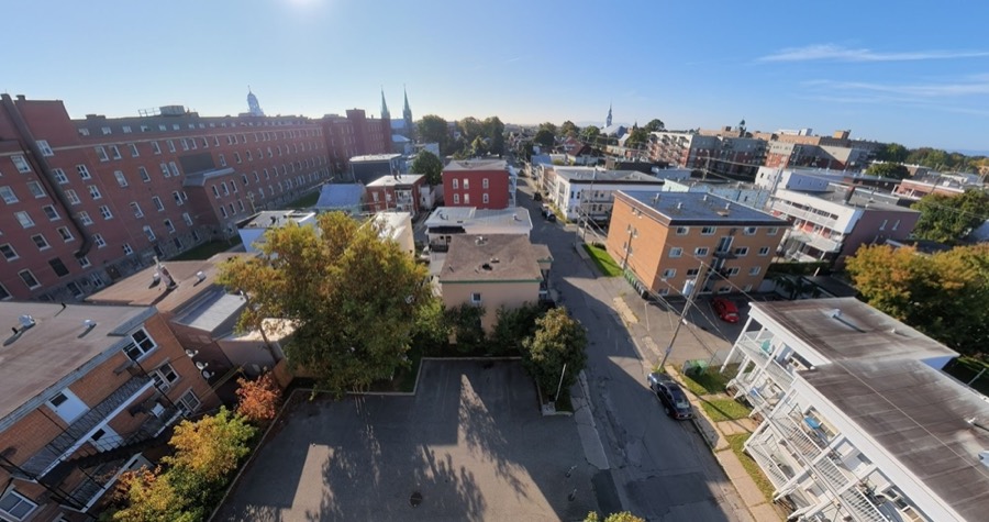 Vue aérienne d'un stationnement et d'une rue de quartier, avec des clochers à l'horizon